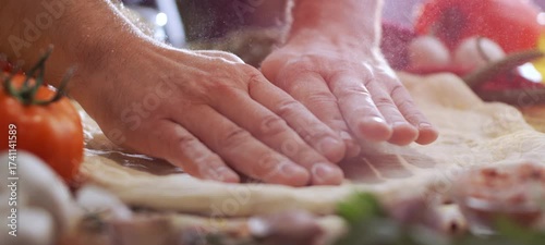 Male chef hands kneading raw pizza dough on a wooden table, sprinkling it with flour, getting ready to prepare a traditional italian meal in a restaurant kitchen with fresh ingredients