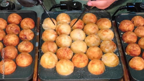 A chef is grilling and rotating golden, crispy takoyaki balls, a beloved street food snack from Japan