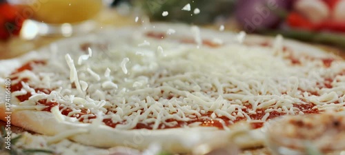 Close-up of a chef sprinkling delicious grated mozzarella cheese over a raw pizza base with fresh tomato sauce, preparing a traditional italian meal in a professional kitchen or pizzeria