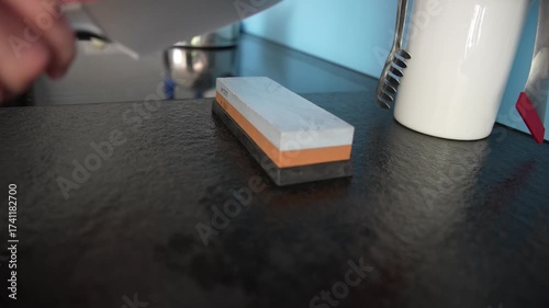 Man in own kitchen sharpening kitchen knife with help of grindstone with 300 hardness grade (blue) and 1000 hardness grade (brown). Movie shot October 4th, 2025, Zurich, Switzerland.