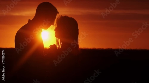 A couple hugging each other at sunset. The silhouettes are emphasized by the contrast of the bright sky and dark figures. Concept love story. Super slow-motion shot.