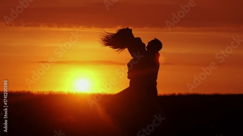 A couple hugging each other at sunset. The silhouettes are emphasized by the contrast of the bright sky and dark figures. Concept love story. Super slow-motion shot.