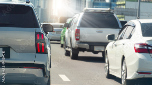 Rear side of luxury car driving the asphalt road. Clear traffic on the road with row of cars in the city. Blurred of town far away in the bright light.