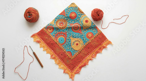 Vibrant Crocheted Shawl with Intricate Mandala Patterns in Turquoise, Orange, and Yellow Tones Beside Yarn Balls and Crochet Hook on White Background