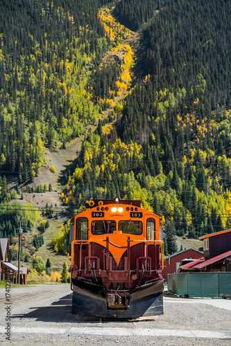 Durango and Silverton narrow gauge steam engine train stop in front of a beautiful mountain view during early fall foliage in Silverton town. Classic railroad transport in Colorado, USA.