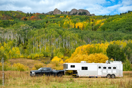 Pickup truck and travel trailer parking among colorful fall foliage of Kebler pass, a scenic mountain pass in the Rocky Mountains near Crested Butte, Colorado, USA. Camping travel in autumn season