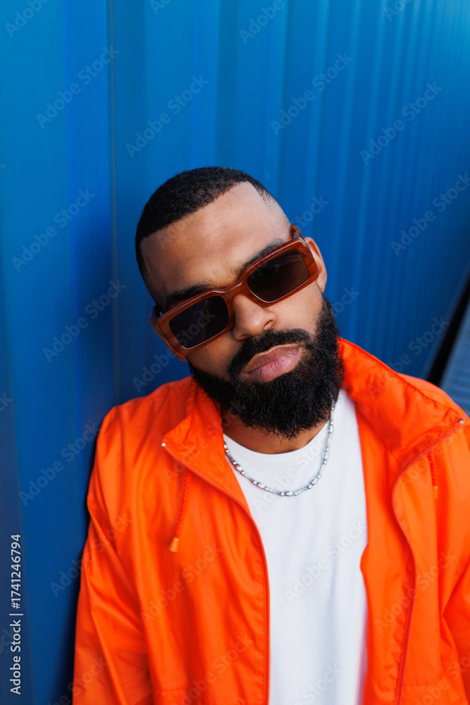Fototapeta premium Portrait of bearded black man in sunglasses and windbreaker jacket posing in port 