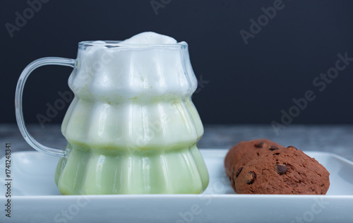 Mug of green coffee and brown cookies on dark background