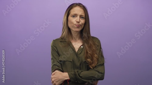 Woman in olive shirt with long hair, pursed lips and folded arms in a studio with purple backdrop; doubt.