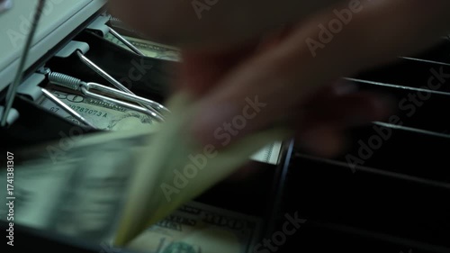 A cashier, holding a dollar bill, opens the cash register and gives out change