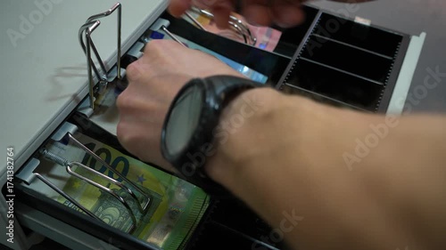 Man's cashier hand opening cash register and taking changing money banknotes