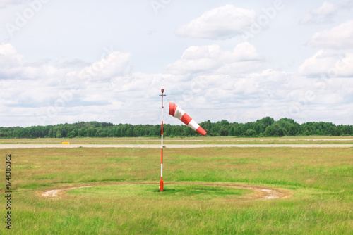 Canvastavla Red and white windsock near runway in a grassy field under a cloudy sky with trees in the background
