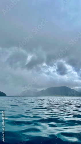 Ocean view under a cloudy sky with mountains in the distance.