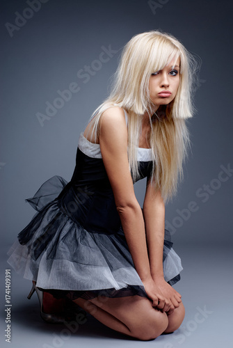 Bild auf Leinwand A fashionable upset sad young woman dressed in a stylish black outfit posing gracefully against a minimalist studio backdrop