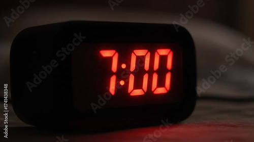 Closeup clock changing to 7:00 AM on digital red LED alarm in dark bedroom - morning routine and wake up time - start of day concept