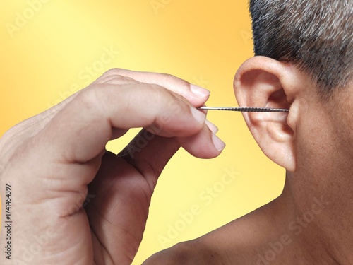 A man is putting ear pick metal, cleaning his ears for healthcare on a yellow background.