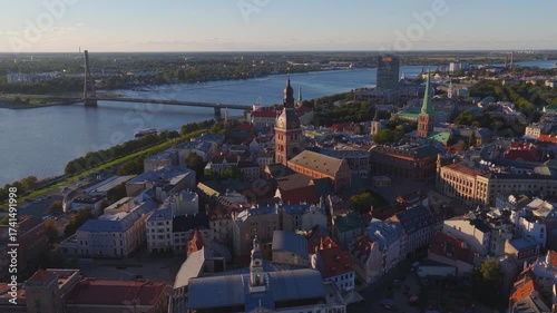 Aerial view of Riga, Latvia, showcasing the old town, Daugava River with a moving boat, a bridge, and the National Library during golden hour.