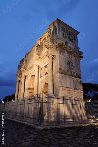 The majestic Arch of Constantine, a famous ancient Roman triumphal arch in Rome, Italy, beautifully illuminated at twilight against a dramatic deep blue evening sky, an iconic travel destination