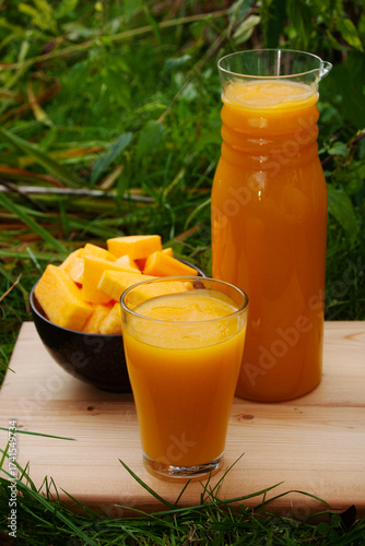 Harvesting fresh pumpkin juice displayed in a glass and pitcher on a wooden board outdoors