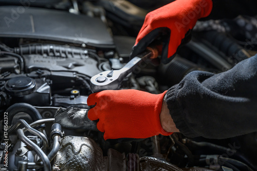 Professional mechanic wearing red protective gloves repairs a car engine under the hood in a modern workshop, showcasing hands-on technical skills, precise tools, and automotive maintenance expertise.
