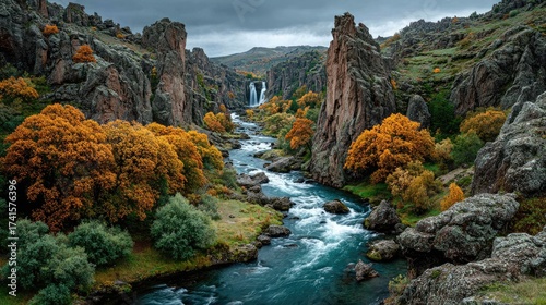 Fototapeta Naklejka Na Ścianę i Meble -  Dramatic river landscape with towering cliffs cascading waterfalls and vibrant autumn foliage under a moody sky