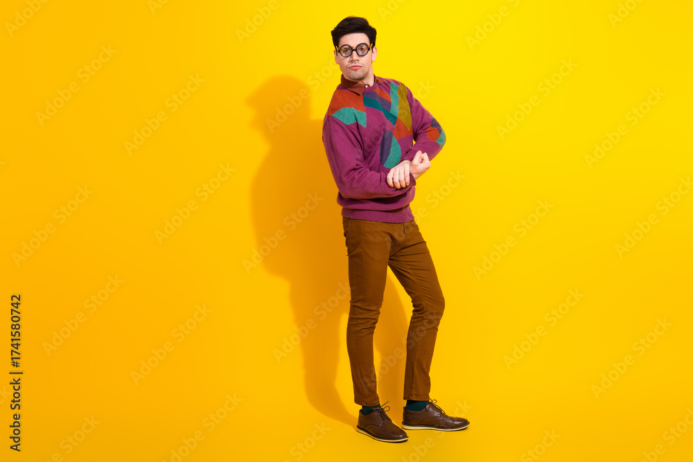 Fototapeta premium Young man with trendy glasses posing confidently in colorful sweater against a vibrant yellow background