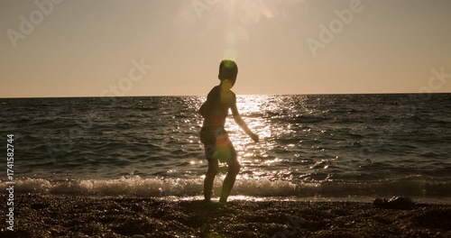 Young boy in silhouette enjoys throwing stones into the ocean at a beautiful sunset.