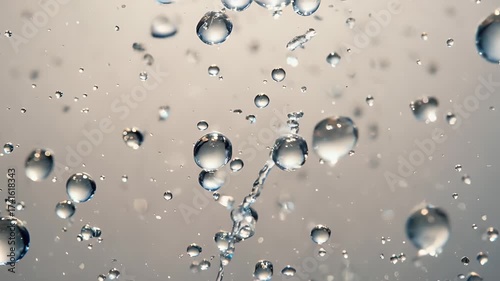 Numerous clear water droplets and bubbles suspended in motion against a light grey background