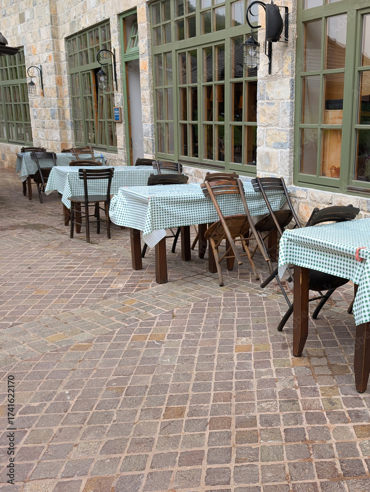 Naklejka premium Rustic outdoor cafe terrace with wooden tables and checkered cloths by a stone building. Social gatherings, hospitality, and cultural atmosphere in Drvengrad.