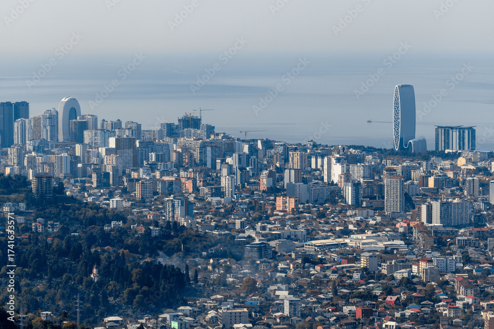 Fototapeta premium A cityscape with tall buildings and a blue sky. Panorama of Batumi from the mountains. Skyscrapers and buildings.
