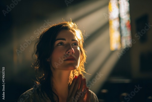 Beautiful woman praying in church with sunlight shining through stained glass window seeking hope and inspiration