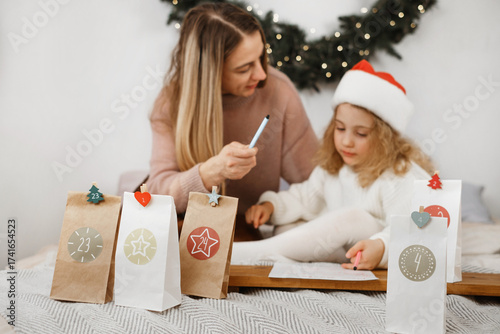 Mother and child writing a letter to Santa together in cozy Christmas bedroom, surrounded by festive decorations, advent calendar, and Christmas tree
