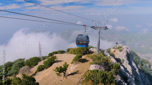 Blue cable car cabins moving high above mountain slopes and clouds at Mount Babadag in Mugla, Turkey. Aerial rope transit, gondola lift. Tourism, sightseeing, and public transportation concept