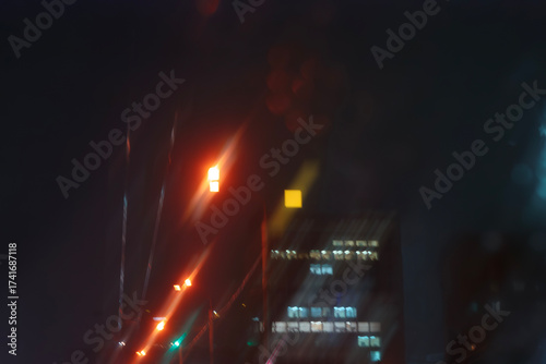 A blurry view of night traffic and streetlights seen through a rainy car windshield.