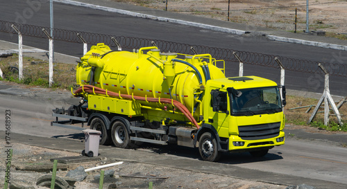 Bright yellow vacuum truck parked on a road near construction. Industrial vehicle used for liquid waste removal, maintenance or cleaning services
