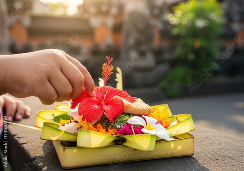 Child's hand preparing a traditional Balinese Canang Sari offering with flowers at a Hindu temple
