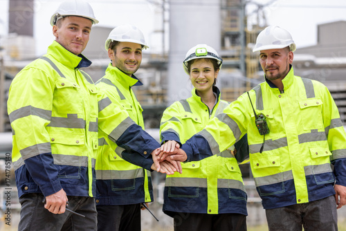 Industrial engineer, workers in a refinery - oil processing equipment and machinery energy factory. Image of engineers put hands on top of each others as symbol of their partnership. 