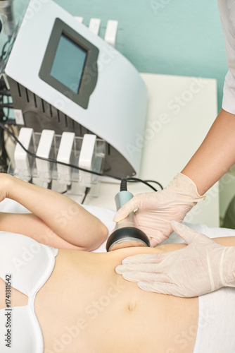Female caucasian adult receiving ultrasound cavitation treatment in spa for body contouring and fat reduction.