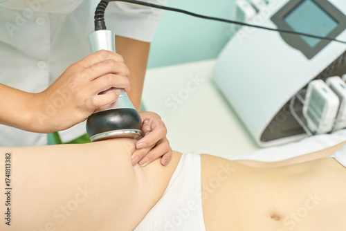 Caucasian female undergoing non-invasive ultrasonic cavitation treatment for fat reduction in medical spa setting.