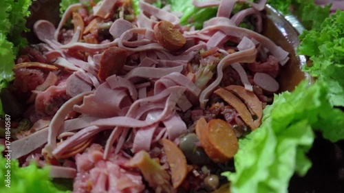 Close-up of a hand dropping chorizo slices over the curtido and cold cuts of Guatemalan fiambre. Scene representing the artisanal preparation of this traditional All Saints’ Day dish.