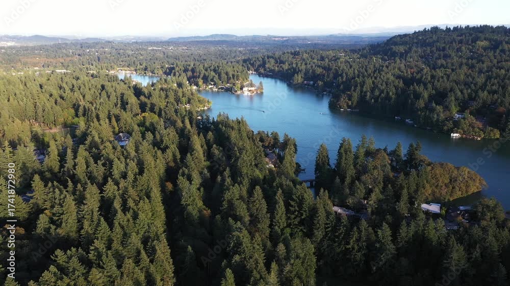 4K aerial drone footage of Lake Oswego, Oregon, showing calm blue water surrounded by dense forest and residential homes on a clear sunny evening. Captured during earl fall season from high altitude.