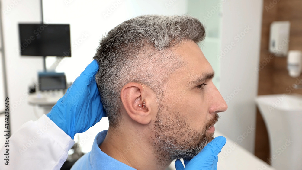 Fototapeta premium Doctor audiologist applying hearing aid to mature man's ear. Hearing-impaired man needs hearing aids