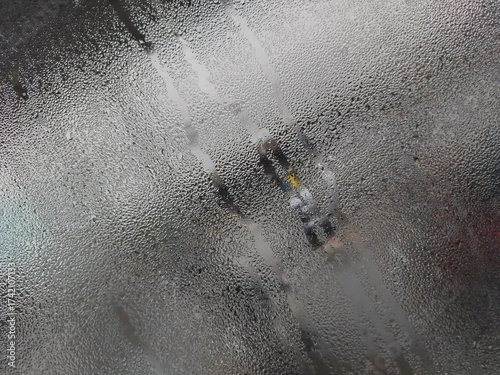 A close-up of a windowpane completely covered in tiny condensation droplets, with vertical streaks and a muted grey quality.