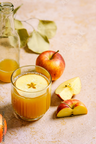 Ein Glas frischer Apfelsaft und rote Äpfel auf einem rosa Tisch. Herbst, Getränk.