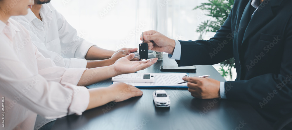 © doidam10 - Panorama view of car dealer handing key and vehicle model to customer during contract signing, concept of auto loan, finance, leasing, insurance, purchase agreement and business success. auto loan.