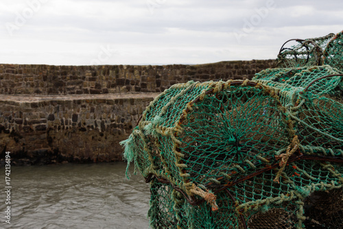 Green lobster pots stacked on quay in harbour