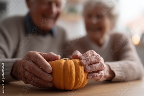 Senior couple admiring a small orange pumpkin on a table with their hands in a bright indoor setting