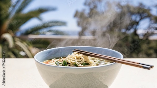 Steaming bowl of noodles with fresh greens by the sea