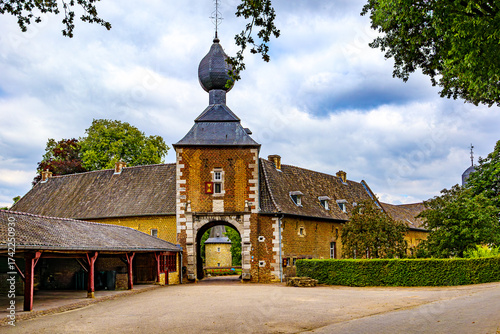 Front view of arched entrance to Cortenbach Castle, tiled gable roof and bulbous dome, brick walls, green bushes and leafy trees, cloudy day in Voerendaal, South Limburg, Netherlands
