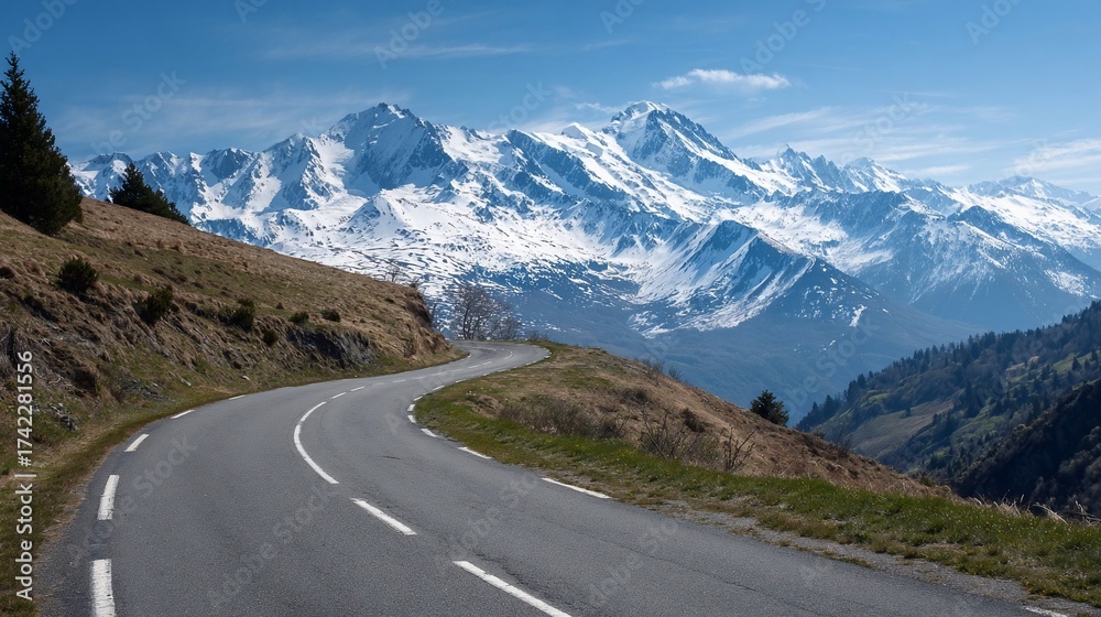 Naklejka premium Scenic mountain road winding up hill towards snow-capped peaks under a blue sky